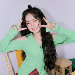 A smiling woman with long dark hair wearing a green top and red plaid skirt, making peace signs with both hands in front of her face.