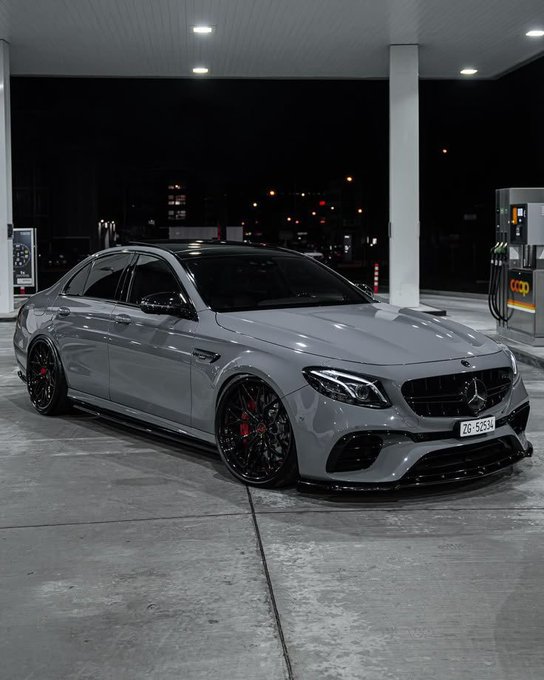 A gray Mercedes-Benz sedan with red brake calipers parked at a gas station at night, license plate visible.
