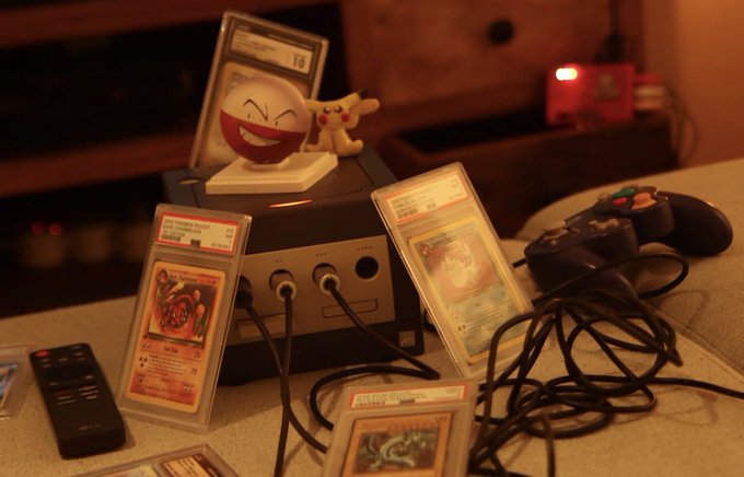 A GameCube console is displayed with Pokémon trading cards in PSA grading slabs and a Pikachu figurine on top, reflecting the "nerdmaxxing" and nostalgic gaming aspect of the post. The caption captures the wholesome, hobby-filled vibe of enjoying collectibles and gaming with friends while maintaining an optimistic outlook on life and crypto markets.