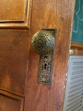 An ornate brass doorknob and decorative backplate adorn a wooden door, showcasing the intricate craftsmanship typical of historic buildings. The detailed metalwork exemplifies the timeless elegance referenced in the post, where such thoughtful touches transform a space and give it a distinctive, almost palpable atmosphere.