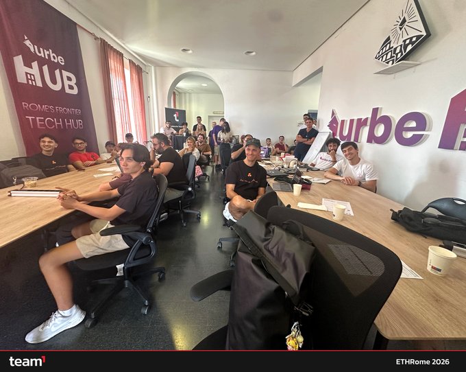 A group photo of attendees seated at long tables in the 'Würbe Hub - Rome's Frontier Tech Hub,' with people working on laptops in what appears to be a co-working event space, labeled 'ETHRome 2026' at the bottom.