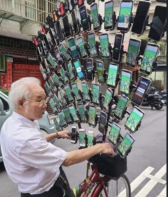 An elderly man riding a bicycle loaded with an enormous cluster of smartphones mounted around him, all displaying a mobile game on their screens.
