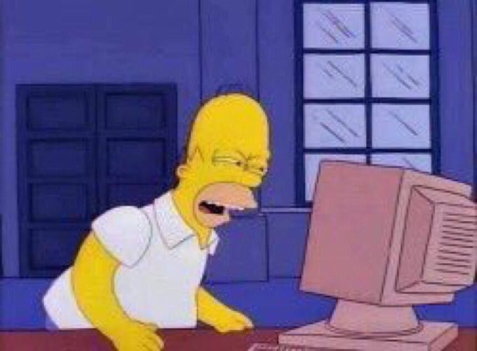 A cartoon still of Homer Simpson looking frustrated and yelling while working at a computer desk.