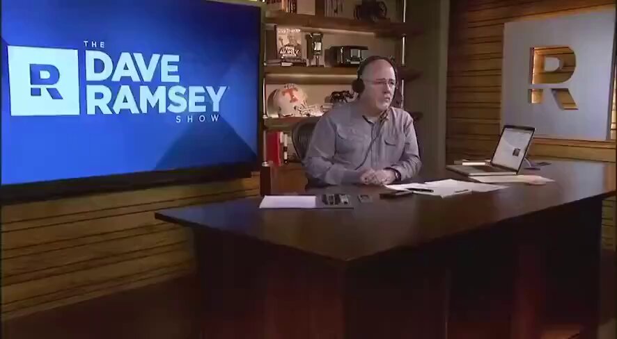 The image shows a man seated at a desk with a computer monitor displaying the Dave Ramsey show, which includes information about Bitcoin. The Bitcoin price has reached over 22,000% since Dave Ramsey made his statement about it being "a really good way to turn $1M into nothing". A laptop is also visible on the desk in front of the man.