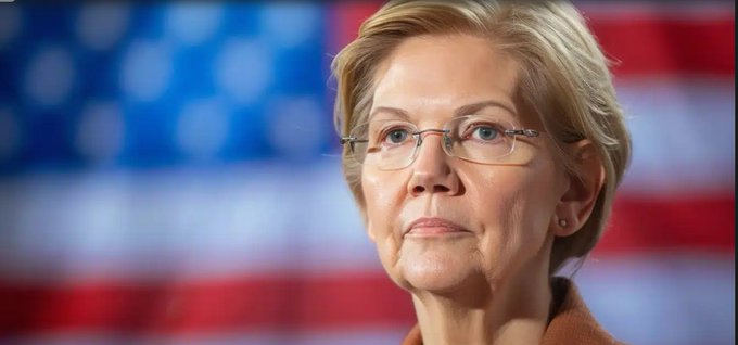 A close-up portrait of U.S. Senator Elizabeth Warren wearing glasses, with an American flag blurred in the background.