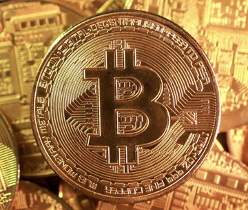 A gold-colored physical Bitcoin token rests atop a pile of similar coins, with inscriptions like "BITCOIN DIGITAL DECENTRALIZED PEER TO PEER" and "FINE COPPER" visible around its edge. The image relates to the post about spot Bitcoin ETF inflows, as it visually represents Bitcoin, the underlying asset of the ETFs mentioned, including BlackRock's IBIT, Fidelity, and others, which saw $4.9 million in net inflows.