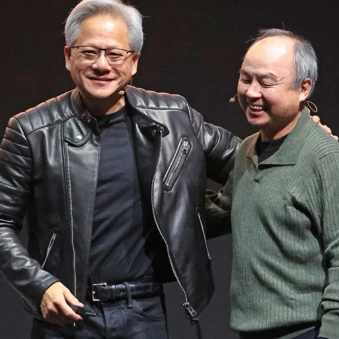 The image shows two men standing next to each other, both wearing leather jackets. One man has gray hair while the other has black hair. The man with gray hair appears to be smiling at the camera, while his companion looks at him. They are positioned in front of a dark background, which contrasts with their attire and makes them stand out.