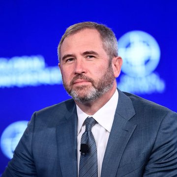 Ripple CEO Brad Garlinghouse appears on stage at a Milken Institute event, wearing a dark suit and patterned tie with a lapel microphone, as he discusses the recent failure of the CLARITY Act vote and its implications for crypto regulation.