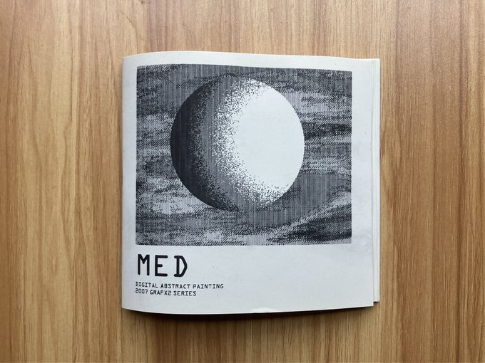 A folded zine or small publication titled 'MED - DIGITAL ABSTRACT PRINTING, 2007 GRAFX SERIES' rests on a wooden surface, featuring a black and white halftone illustration of a sphere against a textured background.