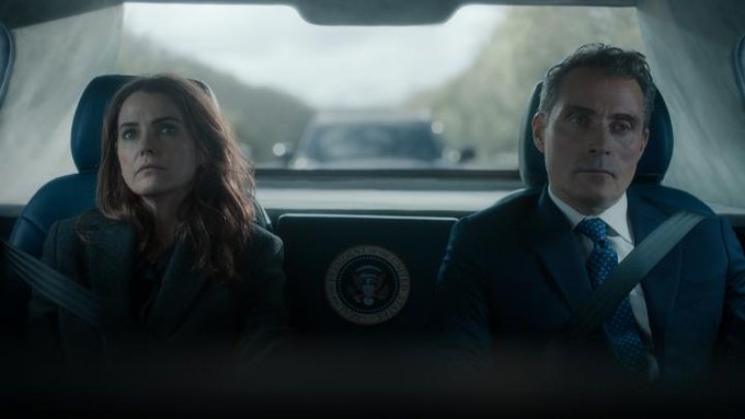 A woman and a man in a suit ride in the back of a vehicle featuring the Presidential Seal of the United States, with the post "we are at unreal levels of back rn" humorously playing on the idea of being in the presidential limousine ("the back").