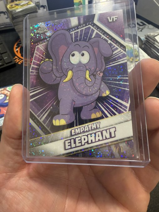 A hand holding a holographic trading card in a protective sleeve featuring a cartoon purple 'EMPATHY ELEPHANT' with 'VF' marked in the corner.