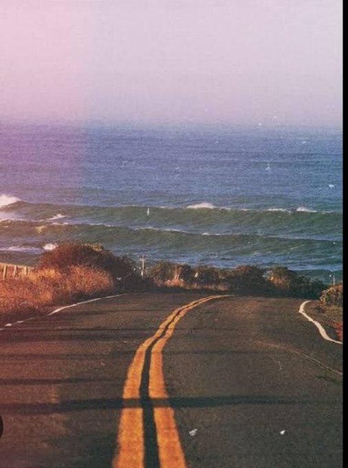 A coastal road with double yellow lines curves toward the ocean under a hazy sky, evoking a quiet, reflective journey—mirroring the post's theme about taking a different, more grounded path in Web3 recognition.