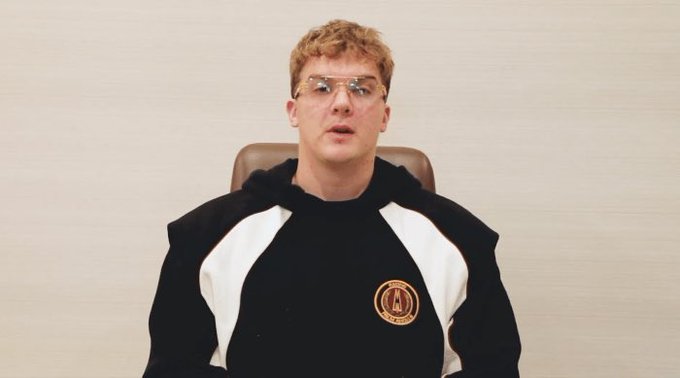 Hayden Adams, founder of Uniswap, sits wearing a black and white hoodie with a gold emblem, appearing calm and composed during what looks like an interview setting.