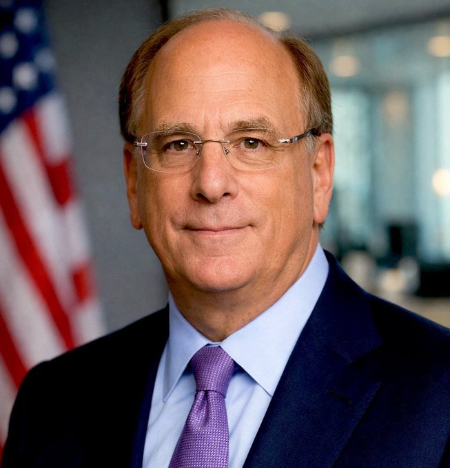 An official portrait of a balding man wearing glasses, a navy suit, and purple tie, with an American flag in the background.