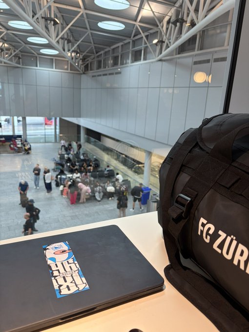 A laptop and an "FC ZÜRICH" duffel bag sit on a counter overlooking an airport terminal, with a "Big Shift" sticker on the laptop—capturing the moment before heading out to Belgrade for the Belgrade Blockchain Week and Solana Summit events.