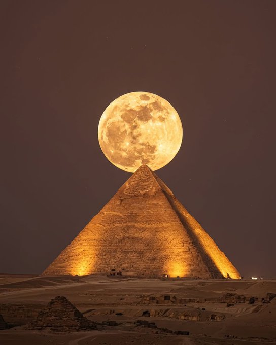 A massive glowing full moon appears perfectly balanced atop the illuminated peak of an Egyptian pyramid, likely the Great Pyramid of Giza, under a dark amber sky — a dramatic visual metaphor suggesting XRP's ascent toward an extraordinary, "moon-like" target.