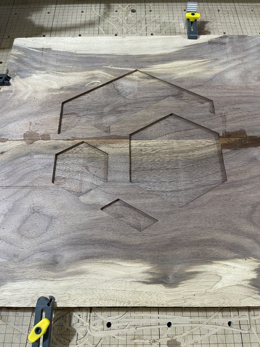 A woodworking project shows a piece of wood with geometric shapes (triangles and a diamond) cut out of it, clamped to a workbench with a saw cut visible across the middle.