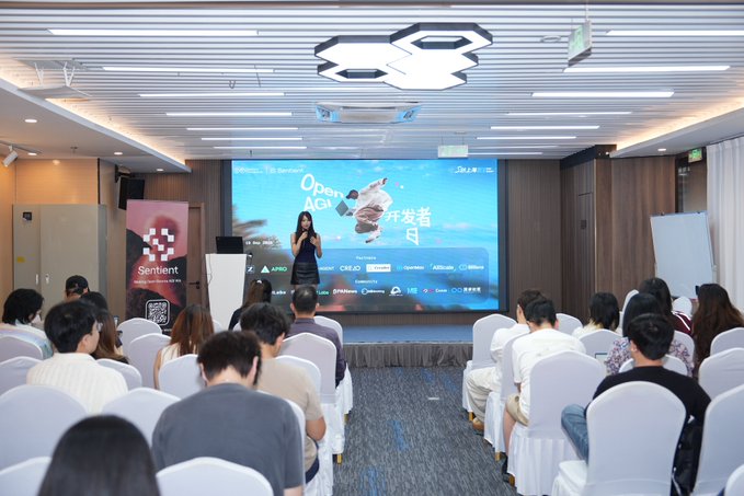 Photo of an Open API conference with a female speaker on stage in front of a seated audience, featuring sponsor logos like Sentient, Alibaba Cloud, and others.