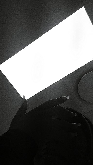 A black-and-white low-light photo of a person's silhouetted hand reaching toward a bright rectangular screen or monitor.