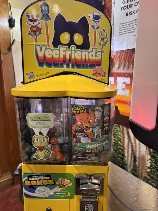 A yellow 'VeeFriends' branded gumball/capsule vending machine displays characters like 'Iguana' and invites users to 'COLLECT THEM ALL!' for 50 cents.