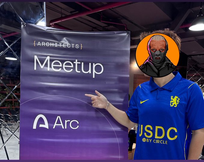 A person in a blue Netherlands national team jersey (with USDC by Circle sponsor) pointing at a purple '{ARCHITECTS} Meetup' banner featuring the Arc logo, with their face obscured by a horror mask avatar.
