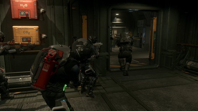 A video game screenshot showing armored soldiers in a dark industrial corridor, with red fire extinguisher boxes labeled 'H₂O' and 'CO₂' on the wall.