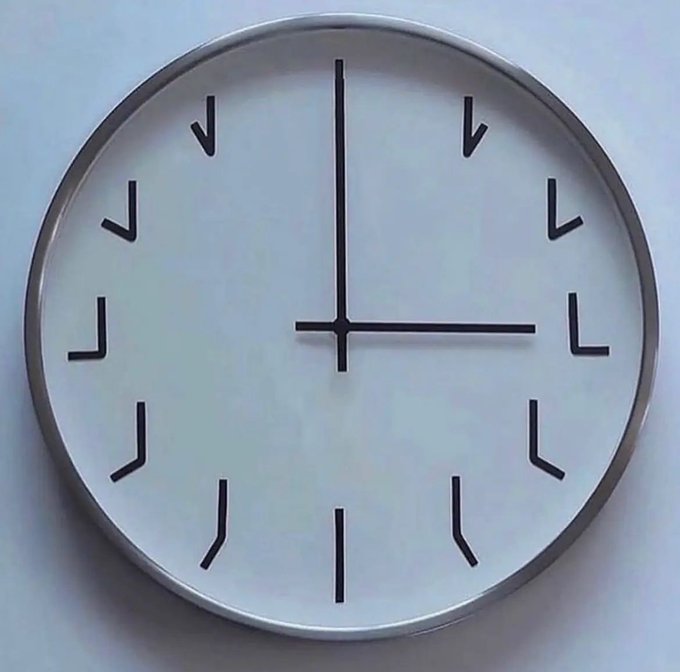 A minimalist round wall clock with simple black bracket-style hour markers and straight hands indicating approximately 3:00.