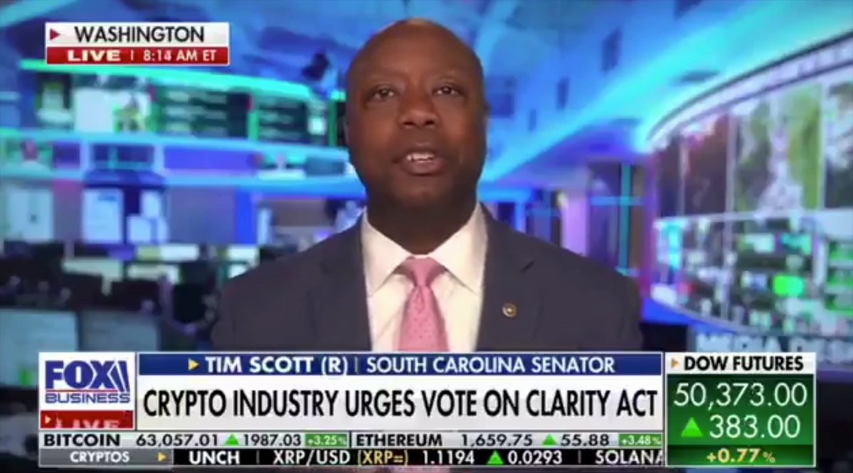 The image shows a man wearing a suit and tie speaking into a microphone during an interview or news broadcast. The focus of the image is on him, with the background blurred out, making him the main subject. The text "TIM SCOTT CLARITY IS COMING! Senate Banking Chairman Tim Scott just dropped the hammer - floor vote on the Digital Asset Market Clarity Act before summer recess!" highlights a significant event or development related to cryptocurrency and the Senate's role in regulating it.