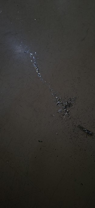 A dark photograph shows what appears to be scattered debris or small objects forming a streak across a scratched, dark surface, possibly viewed through a window at night.