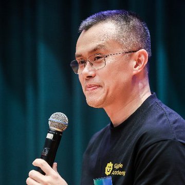 The image features a man wearing glasses, holding a microphone with both hands while standing against a green curtain backdrop. The caption of the image reads "CZ Binance: You don' t have to do anything. HODL." This suggests that the man is likely speaking at an event or addressing an audience related to cryptocurrency and financial markets.