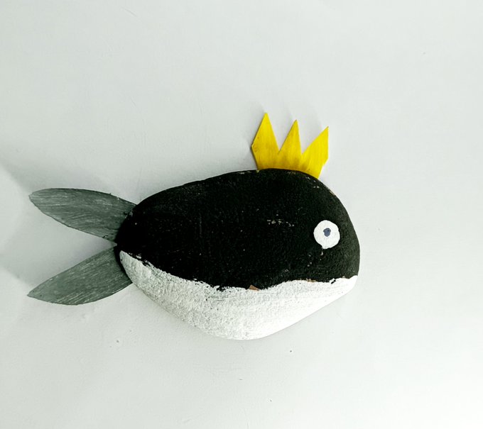 The image features a black and white fish-shaped rock with a yellow crown on its head, giving it an oceanic theme. The rock is positioned against a plain white background, making it stand out prominently. The caption of the image reads "New Drop Ocean Crown 1/1 @TransientLabs minimum bid 0.07 ETH".