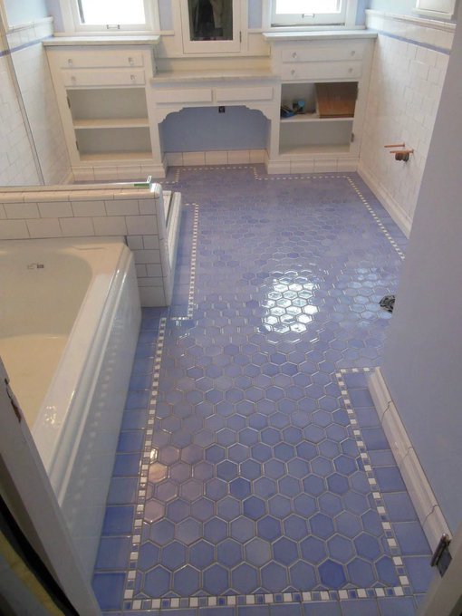 A vintage-style bathroom with light blue hexagonal tile flooring accented by white tile borders, white walls, and a built-in bathtub and vanity.