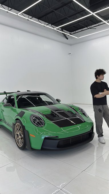 A man stands proudly next to a vibrant green Porsche 911 GT3 RS, likely a new purchase, echoing the boastful "You bought $ANSEM" caption by showcasing a luxury lifestyle symbol.