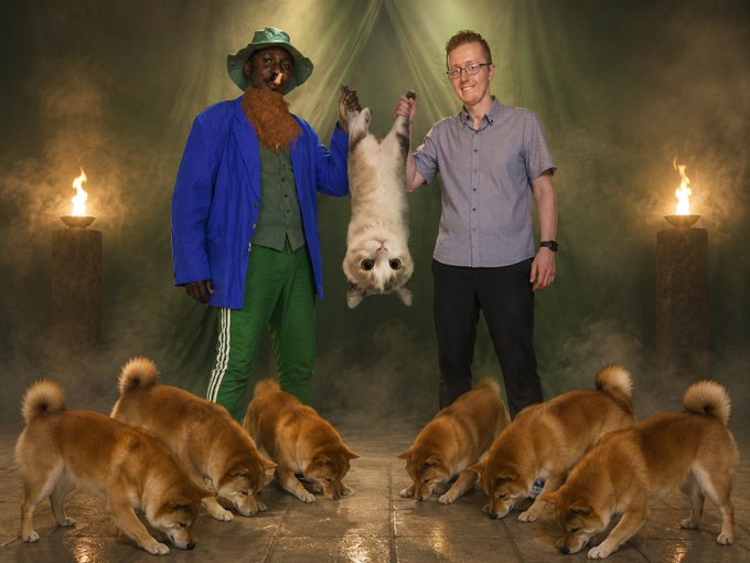The image features a man holding a dog upside down, surrounded by several other dogs of various breeds. The scene takes place in front of a group of lit candles, creating an atmospheric setting for this unusual event. The caption reads "Like $HPOS10i (ticker $BITCOIN) had @BitcoinObama, so do we have our very own vanilla edition: Formerly known as Helmer_Hodl, @StablecoinOsama emerges to save every $SHIB and every $DOGE with an UpSideDownCat! ALL HAIL $USDC!".