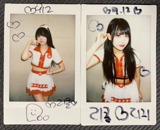 Two Polaroid-style photos side by side showing a young woman with long black hair wearing a white and red nurse-themed outfit, with handwritten dates "09.12" and "09.12" along with doodles of hearts and faces drawn in blue marker on the white borders.