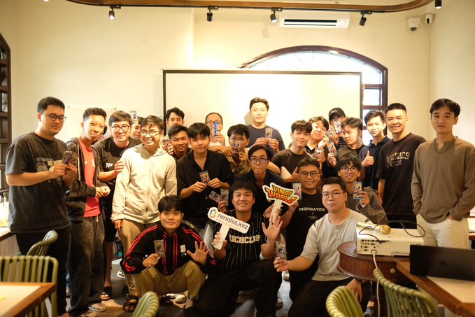 Group photo of around 20 young people posing together in a room, with some holding cards that appear to say 'TenaflyVarc' and 'New World'.