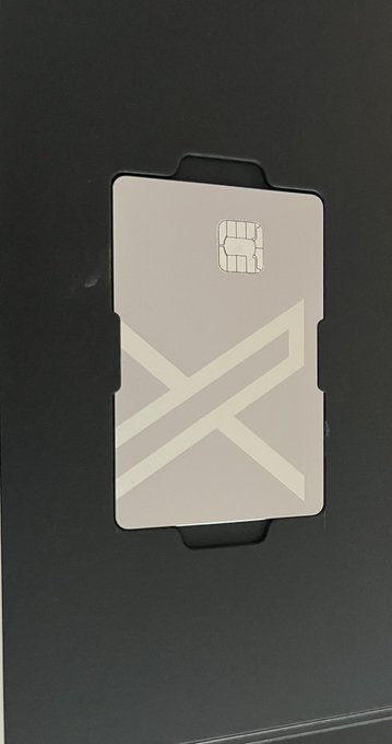 A minimalist white SIM card with a metallic X design and chip, held in a black SIM tray.