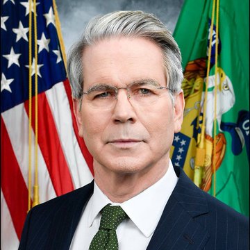 An official portrait of Jerome Powell, the U.S. Federal Reserve Chairman, wearing a dark suit with a green tie, posed in front of the American flag and another official flag.