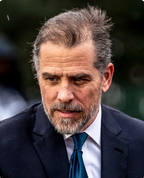A close-up portrait of actor Mel Gibson in a black suit and teal tie, with gray hair and a beard, looking downward with a serious expression.
