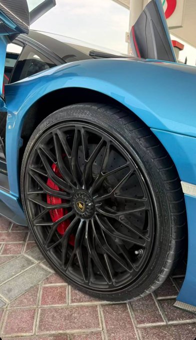 A close-up shot showcases the sleek black multi-spoke alloy wheel and red brake caliper of a blue Lamborghini, likely an Aventador, with the Lamborghini emblem visible on the center cap. The image highlights the high-performance aesthetic of the supercar, fitting the context of a "GM" post expressing enthusiasm for following the user in return for a reply.