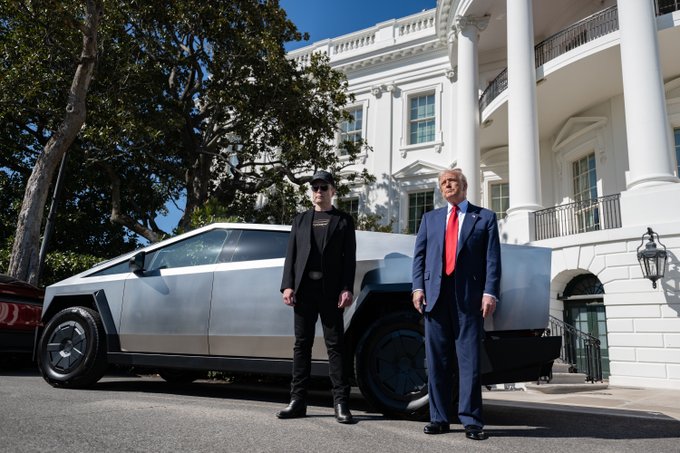 A photograph showing Elon Musk and Donald Trump standing together in front of a silver Tesla Cybertruck at the White House.