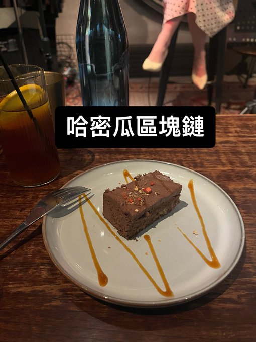 A chocolate brownie dessert on a white plate drizzled with caramel sauce, accompanied by an iced drink, with a Chinese caption '哈密瓜區塊鏈' (Hami Melon Blockchain).