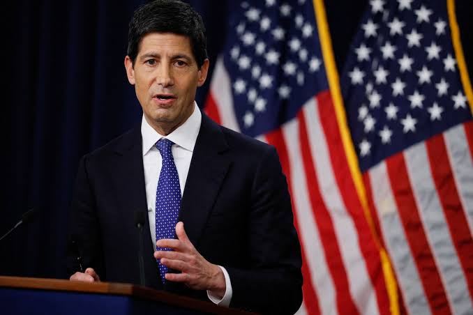 A man in a dark suit and blue tie speaks at a podium with two American flags behind him, likely a U.S. economic or political official providing commentary on the jobs market. The image relates to the post by visually setting the scene for the Non-Farm Payrolls (NFP) discussion, emphasizing the importance of upcoming U.S. employment data and its potential impact on markets like Bitcoin.