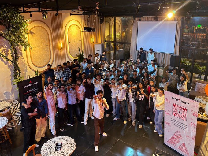 A large group of people poses for a photo at an indoor event, with banners reading 'Builder Hub' and 'team india' visible alongside a QR code.