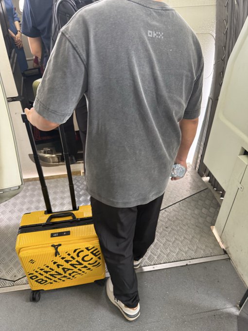 urn of water, black suitcase with yellow letters, and a man's gray t-shirt are present in the image.
