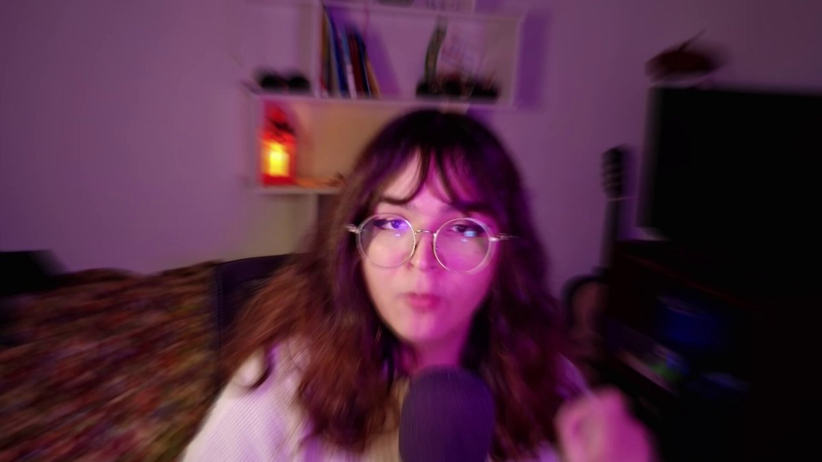 The image features a woman wearing glasses, sitting down and holding a microphone. She appears to be participating in an online gaming event or tournament, as indicated by the text "Extreme & Titan Arena Tournament III is LIVE @VoxieTactics 40,000 $VOXEL prize pool". The woman's position suggests that she might be taking part in a live stream of the event, where her performance can be seen by viewers.