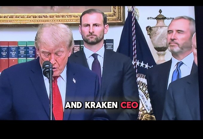 Donald Trump stands at a podium addressing an audience with his head bowed, while Ripple CEO Brad Garlinghouse and another man look on with serious expressions, with on-screen text reading "AND KRAKEN CEO." The caption notes that Garlinghouse appears to have a knowing look, suggesting he may be aware of information not yet publicly shared.