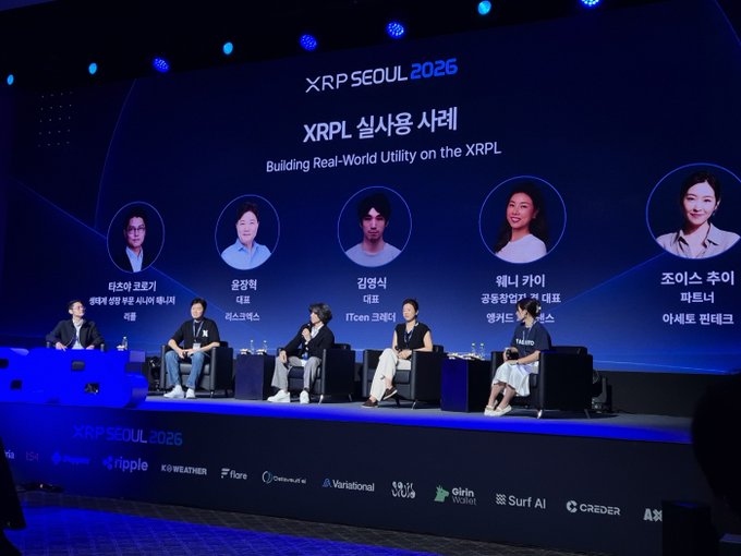 A panel of five speakers sits on stage at the XRPL Seoul 2026 conference, titled 'XRPL 실사용 사례: Building Real-World Utility on the XRPL', with sponsor logos including Ripple, Flare, and DeFiProtocol displayed below.