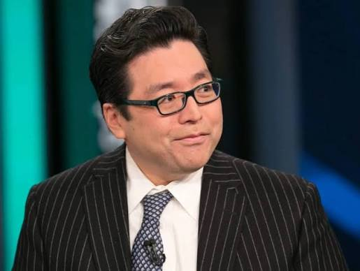 An Asian man with glasses wearing a pinstripe suit and patterned tie appears to be speaking on a news or interview set, likely in connection with the report about Bitmine accumulating 6,000 ETH (worth about $11.2 million) from FalconX, with his attentive expression suggesting analysis of the crypto transaction news.