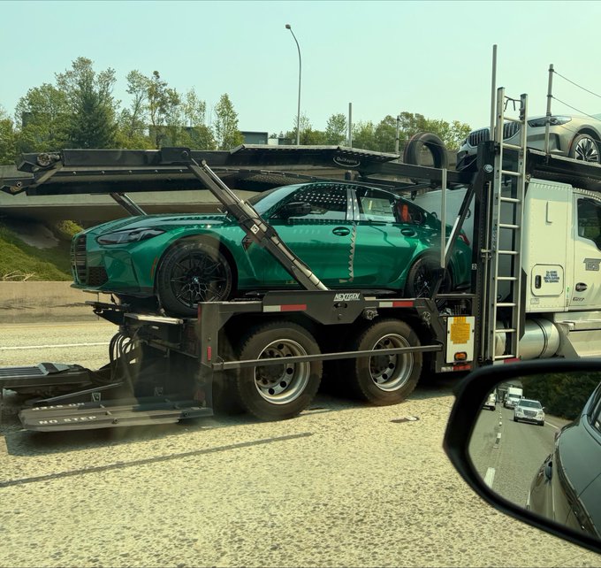 A green BMW M car loaded onto the upper deck of a car carrier truck on a highway.